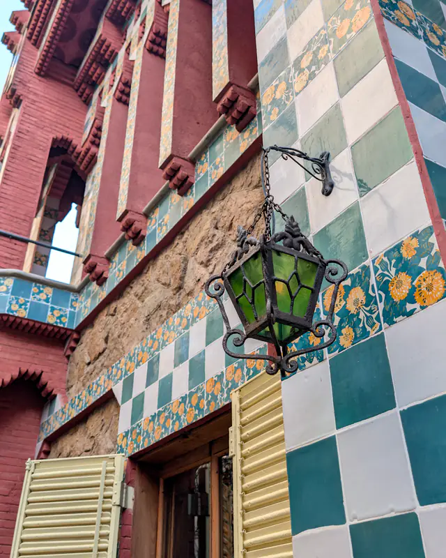 Piastrelle verdi e bianche, mattoni rossi e una lanterna in ferro sulla facciata di Casa Vicens, a Barcellona